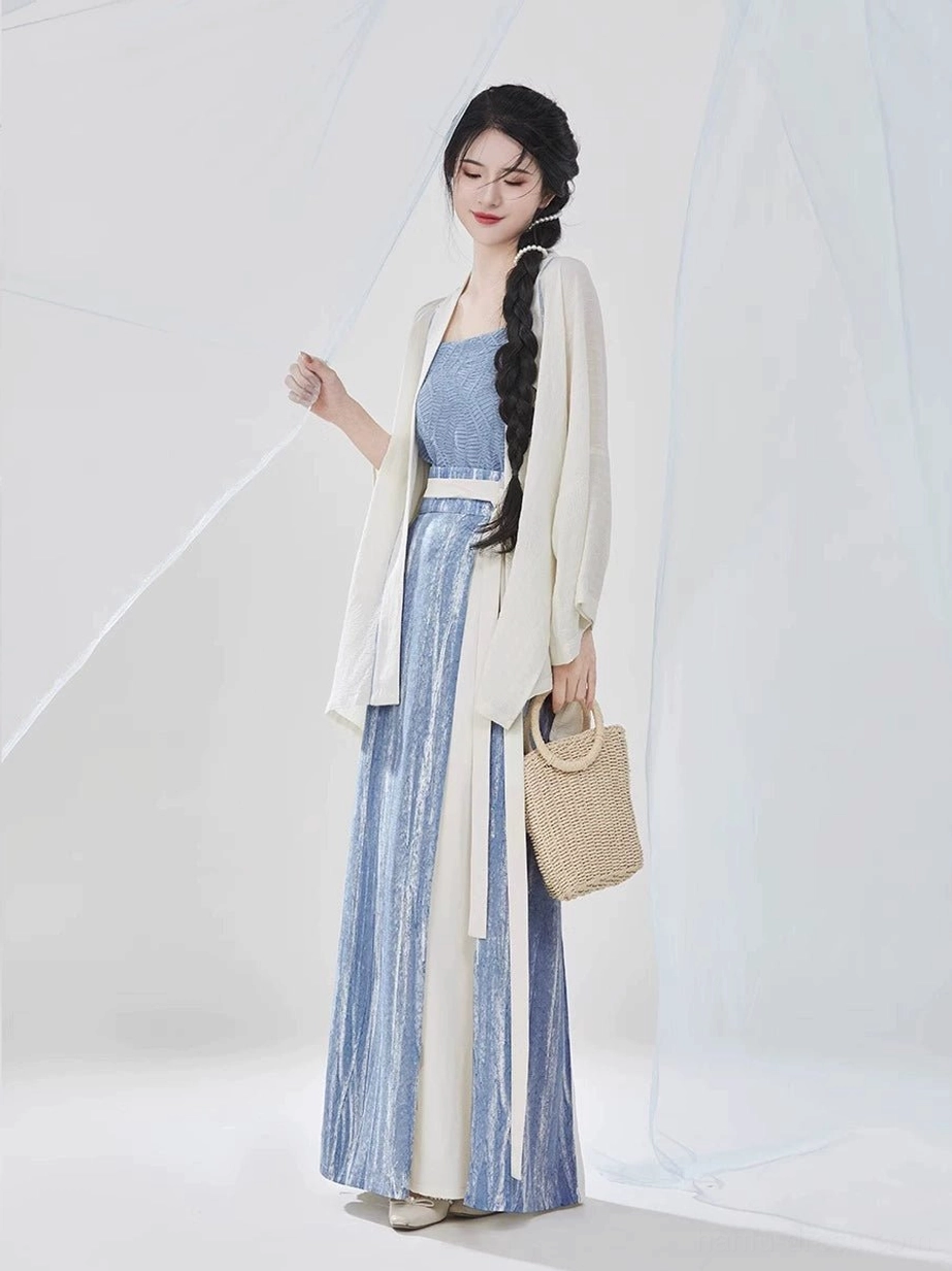 Full-body front view of a woman wearing a Song Dynasty modern Hanfu three-piece outfit with an ivory flowing shirt, sky-blue camisole, two-tone pleated skirt, white waist sash, and woven straw handbag