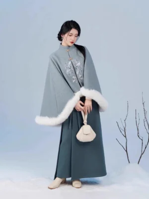 Full-body front view of a woman wearing a Song Dynasty modern hanfu set with dusty blue embroidered cape, white faux fur trim, teal spiral skirt, and classical updo in a snowy winter studio