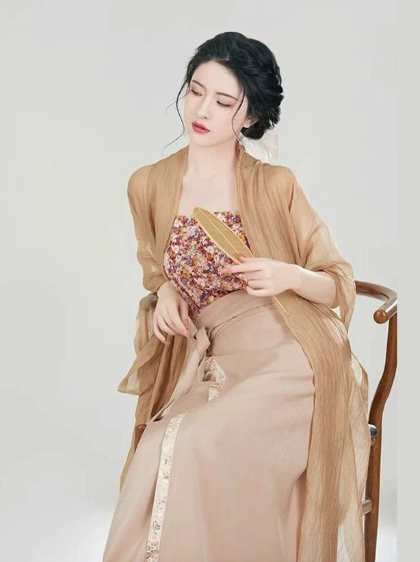 Seated side view of a woman wearing a Song Dynasty modern Hanfu three-piece outfit with sheer beizi jacket, floral camisole, tan wrap skirt, elegant updo, and wooden fan