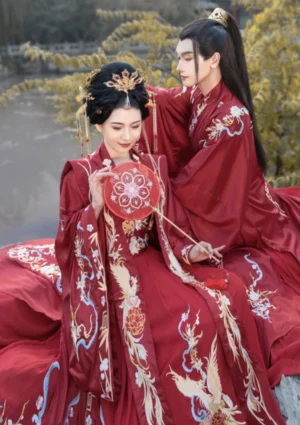 Crimson Chinese wedding hanfu couple by riverside showing phoenix embroidery and embroidered round bridal fan