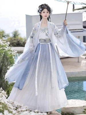 Front full-body view of a woman wearing a blue and white Song Dynasty style qiyao ruqun hanfu with a gradient pleated skirt, embroidered floral details, flowing sheer beizi sleeves, traditional hairstyle, and oil-paper umbrella beside a waterside flower garden