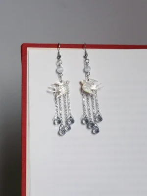 Hanfu swallow tassel drop earrings displayed on a book with white shell swallow charms, silver tone chain tassels and grey faceted pendants