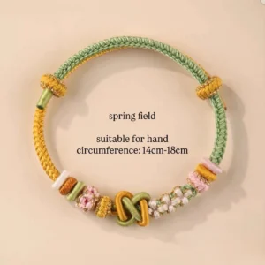 Spring Field handwoven Chinese knot bracelet in pastel green yellow pink and white with floral woven decorations and adjustable double-loop clasp on a light beige background
