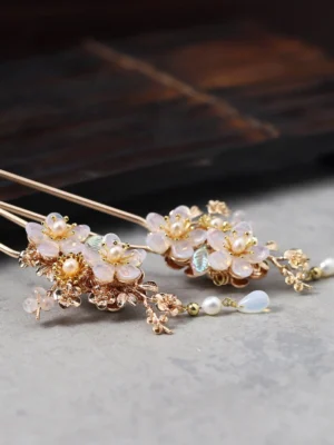 Overhead close-up of a pair of vintage Chinese floral hairpins with gold-tone metal frames, pink flower accents, faux pearls, and opalite teardrop charms for Hanfu hairstyles