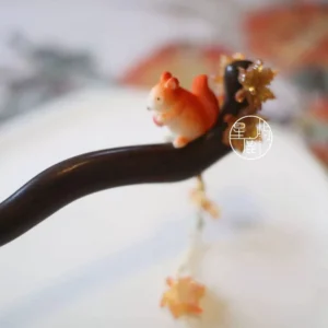 Squirrel and maple leaf Chinese hair stick with dark curved pin, amber leaf ornaments and beaded tassel displayed on a white ceramic plate