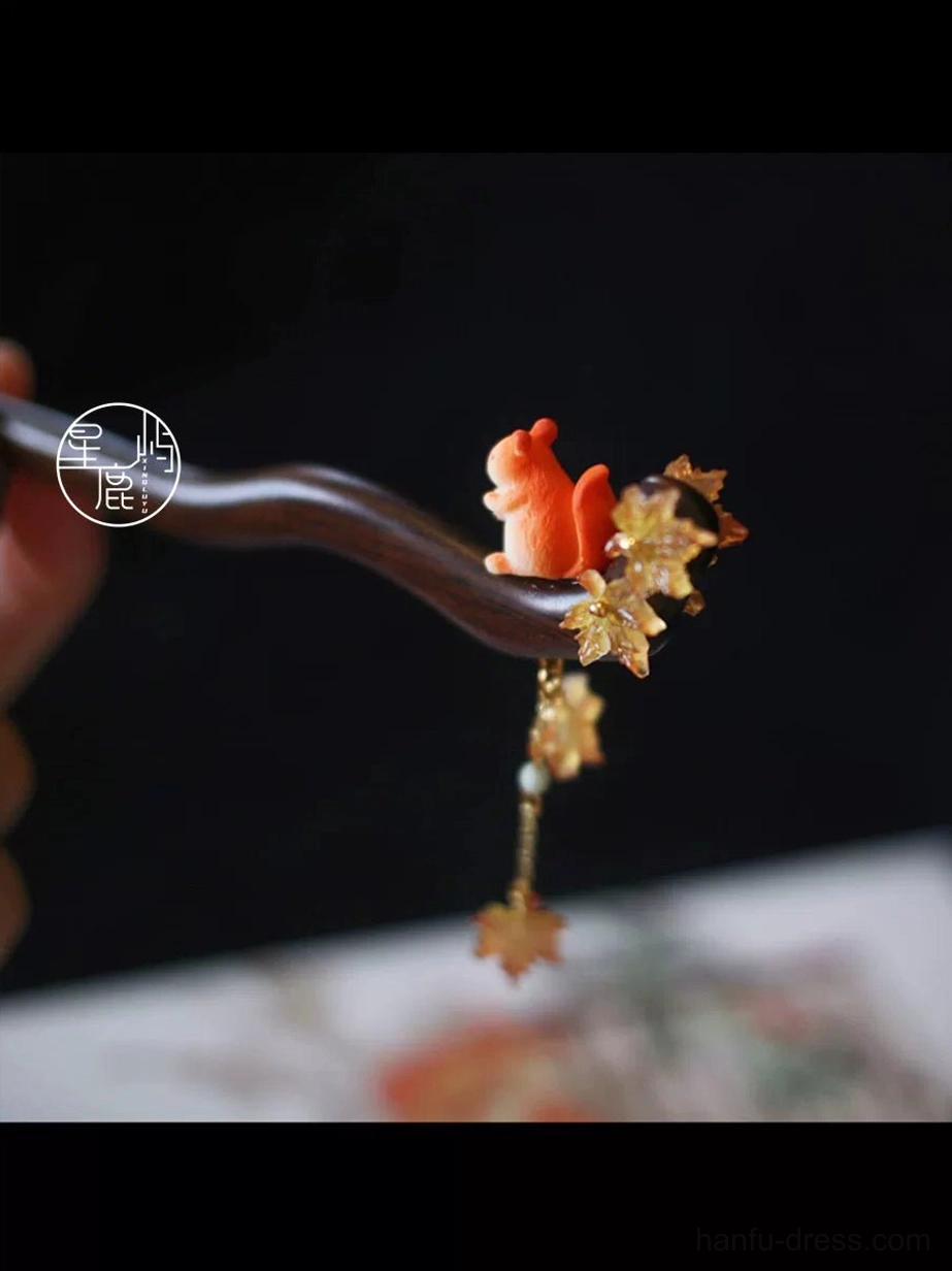 Hand holding squirrel maple leaf Chinese hair stick showing the dark wooden style pin, golden leaf charms and dangling tassel detail