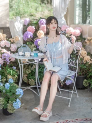 Baby blue modern Song Dynasty Hanfu summer outfit with ruffled cropped camisole, tassel waist shorts, and sheer lace cardigan styled in a romantic hydrangea courtyard