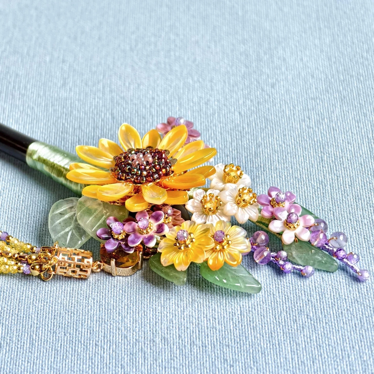 Close-up of sunflower floral decoration on Chinese hair stick featuring resin sunflowers, gemstone-look leaves, gold-tone details and pearl-style tassel beads