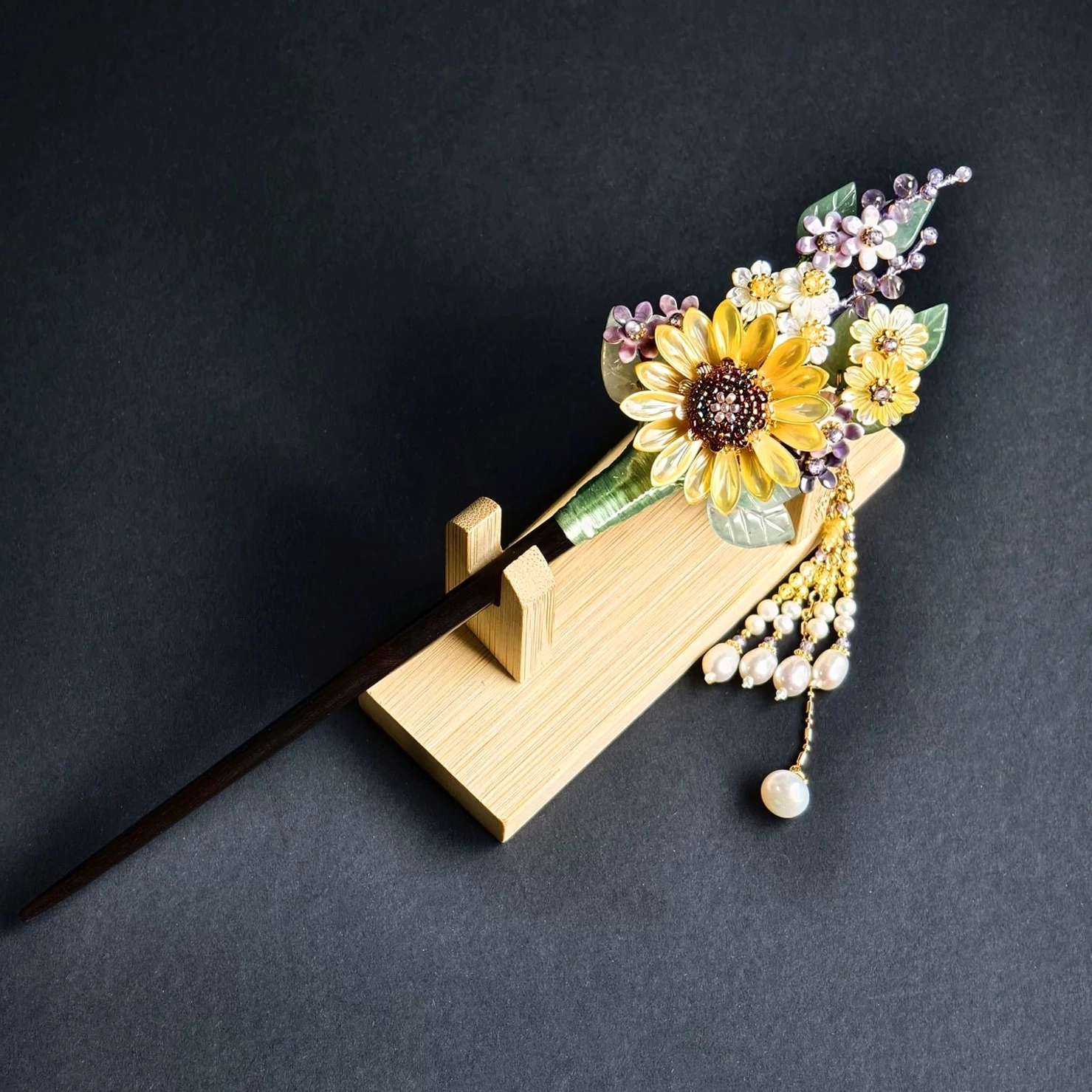 Sunflower tassel Chinese hair stick on a wooden hairpin stand showing the dark brown pin, layered flowers and imitation pearl bead tassel