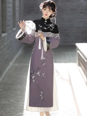 Front full-body view of a dusty purple Swallow's Returns modern Hanfu cheongsam dress with flower-and-bird embroidery, black tassel cape, and white cuffs in a classical Chinese courtyard