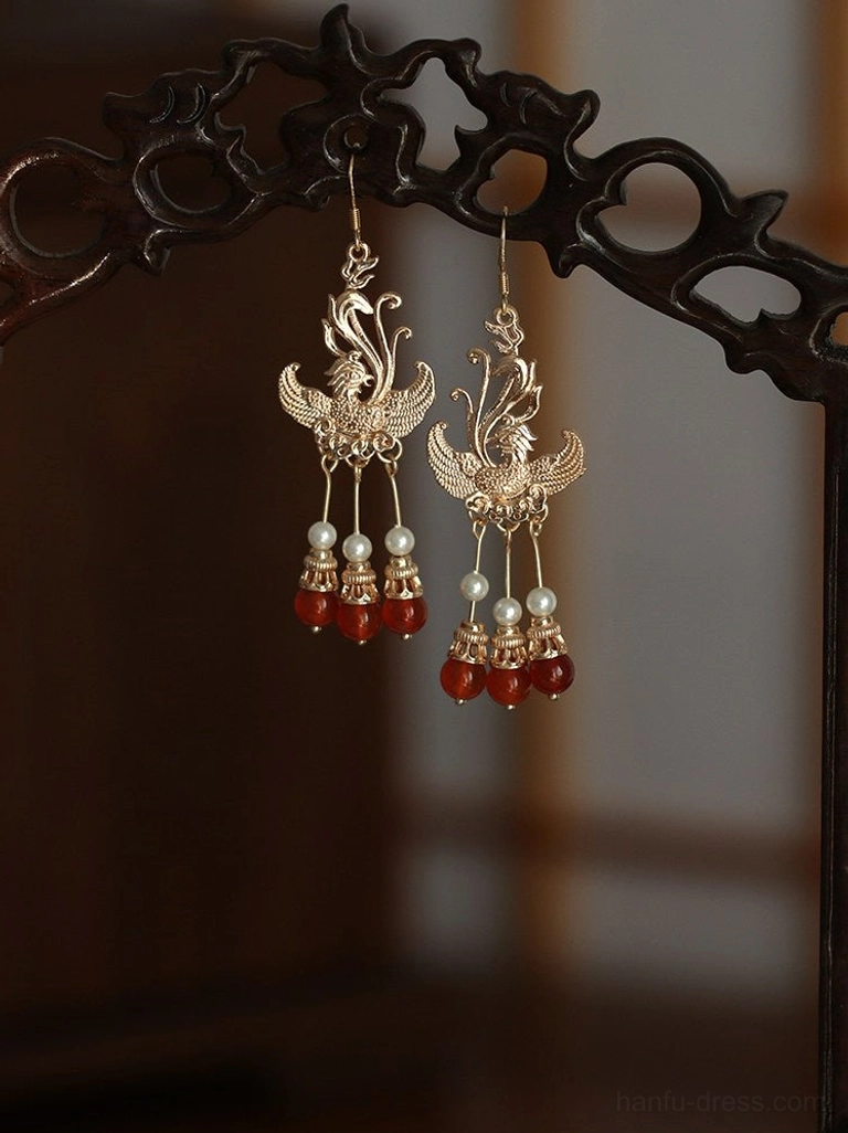 Symmetrical phoenix Chinese earrings with antique gold filigree faux pearls and deep red bead tassels shown on a traditional carved wooden display