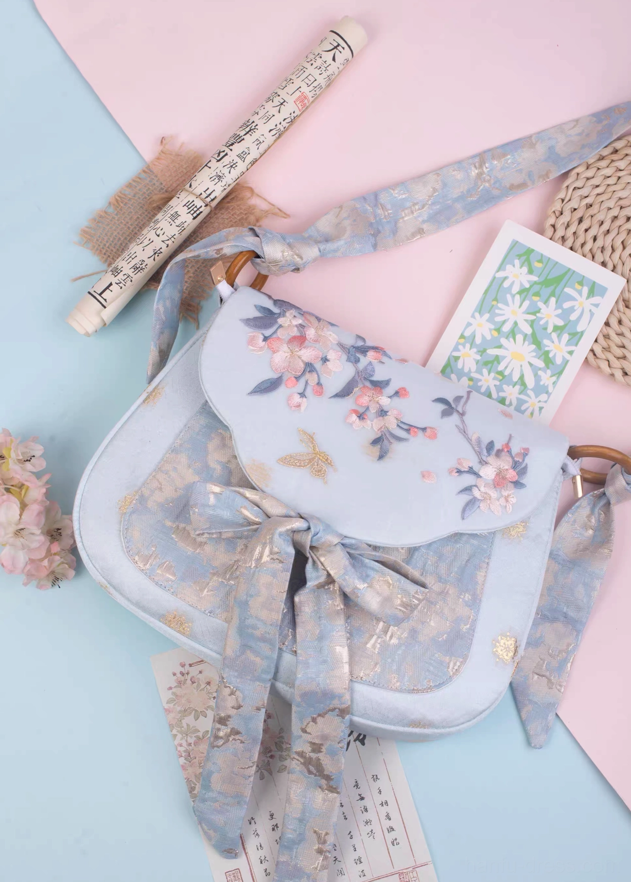 Tang Dynasty inspired sky blue Chinese crossbody bag with pink cherry blossom embroidery golden butterfly motif and jacquard bow strap flat lay view