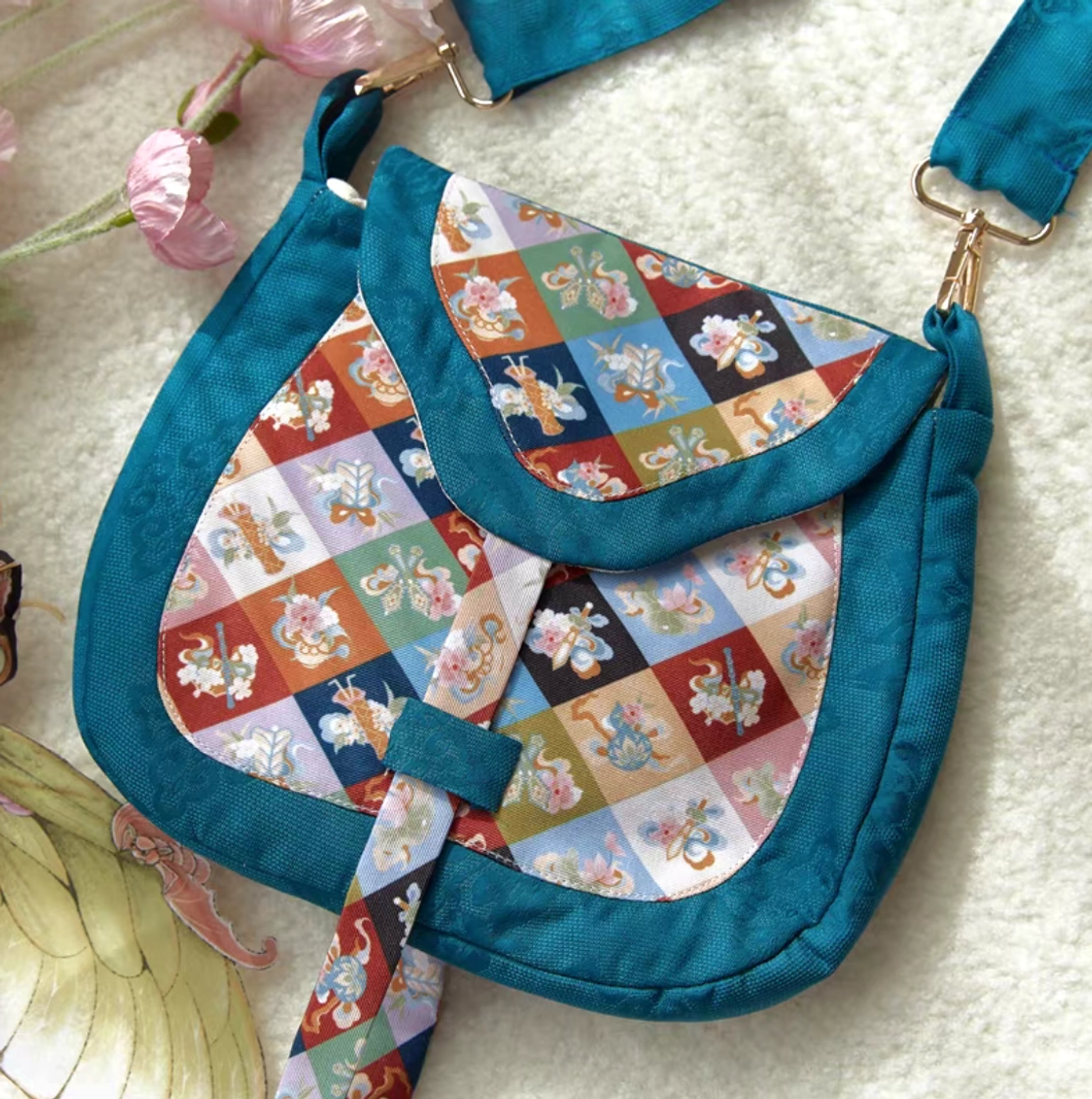 Close-up of Tang Dynasty-inspired Chinese crossbody bag with vivid floral patchwork, teal jacquard canvas frame, decorative strap fastener, and gold metal hardware