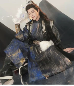 Male model wearing a Tang Dynasty inspired round collar hanfu for men in dark navy and black jacquard fabric with gold dragon embroidery, white fur waist detail, metal arm guards, and decorative belt in a misty mountain studio