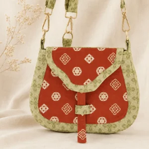 Tang Dynasty floral Chinese canvas crossbody bag shown from the front on linen fabric, featuring a red saddle-shaped body, beige traditional floral motifs, green patterned brocade trim, and gold-tone hardware