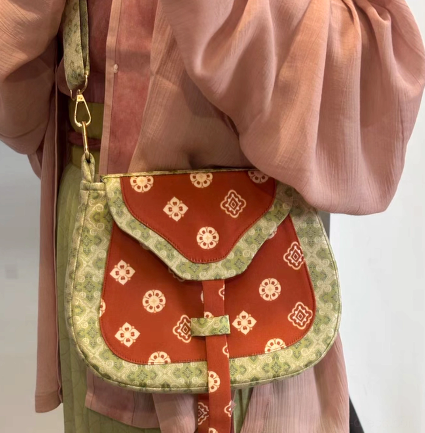 Model wearing a Tang Dynasty floral Chinese crossbody bag with pink Hanfu, showing the compact saddle silhouette resting comfortably at the hip