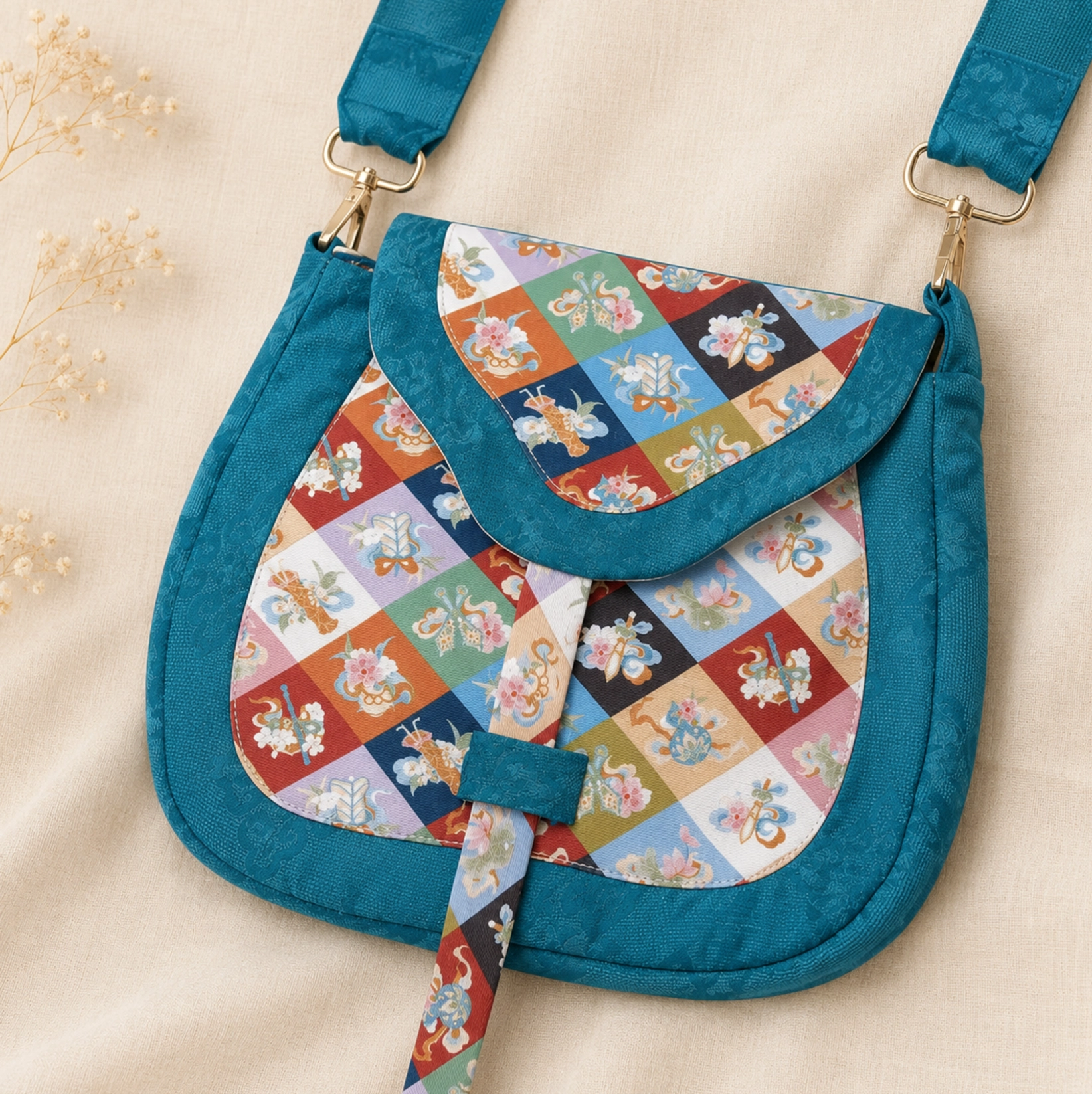 Tang Dynasty-inspired Chinese floral patchwork crossbody bag with teal textured frame, colorful diamond floral panels, gold-toned hardware, and decorative strap on a beige background