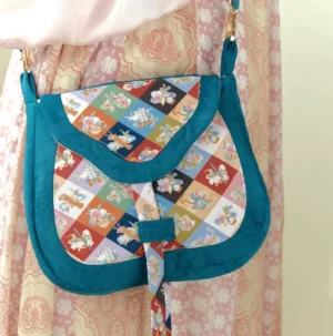 Colorful Tang Dynasty floral patchwork Chinese crossbody bag worn with a pink Hanfu outfit, showing the teal edging, adjustable shoulder strap, and traditional textile details