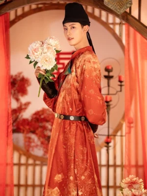 Three-quarter side view of Tang Dynasty groom wedding hanfu in reddish-orange floral round-collar robe with teal embroidered collar and black waist belt