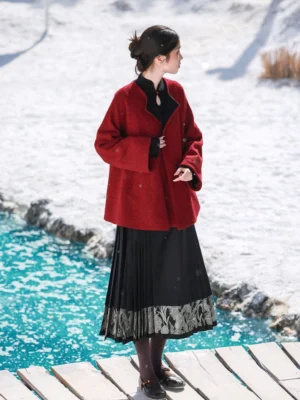 Modern Tang Dynasty hanfu coral red wool blend jacket styled with a black pleated skirt on a snowy lakeside dock