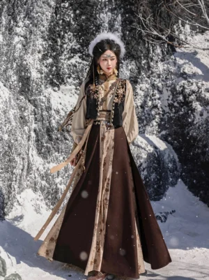 Full-length front view of a Tang Dynasty Hanfu outfit with embroidered vest beige long-sleeve top and flowing color-blocked wrap skirt worn in a snowy mountain setting