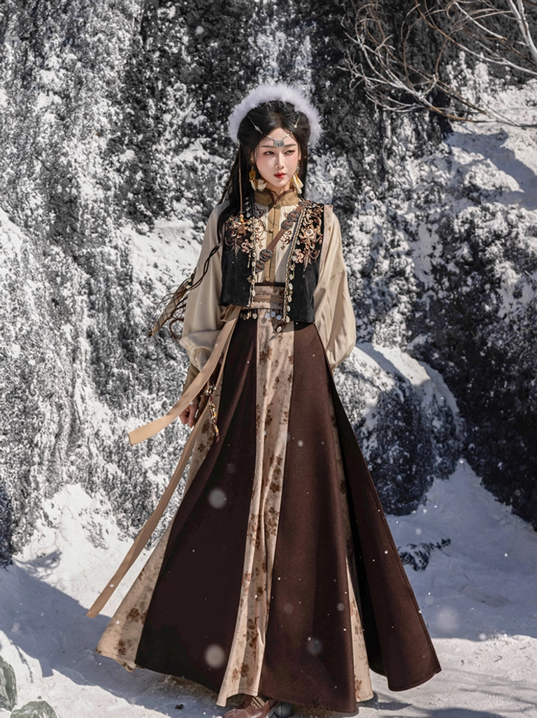 Full-length front view of a Tang Dynasty Hanfu outfit with embroidered vest beige long-sleeve top and flowing color-blocked wrap skirt worn in a snowy mountain setting