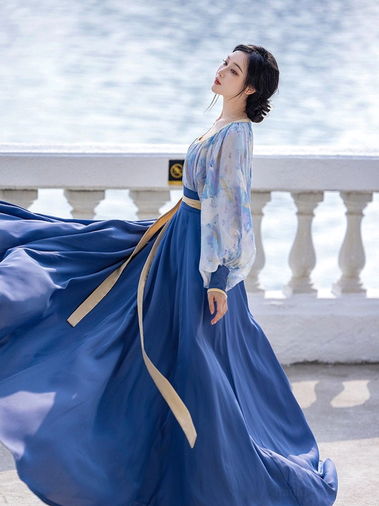 Tang Dynasty Hanfu wrap skirt and printed blouse viewed from the side back with flowing pleats and long beige waist ribbon beside a waterfront