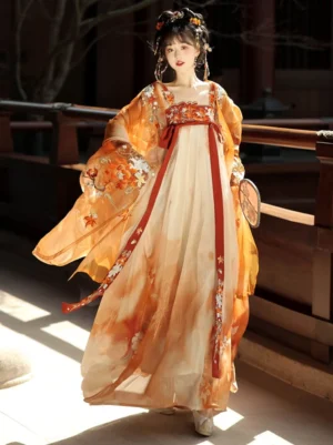 Three-quarter front view of a Tang Dynasty Hanfu Heziqun dress with orange and cream gradient skirt, embroidered red waist sashes, and sheer floral big-sleeve coat in a traditional wooden courtyard