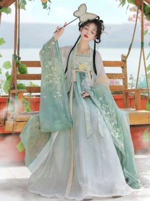 Green Tang Dynasty Hanfu Heziqun complete dress set on model by a lakeside swing, featuring mint green wide sleeves, floral embroidery and light cyan layered skirt
