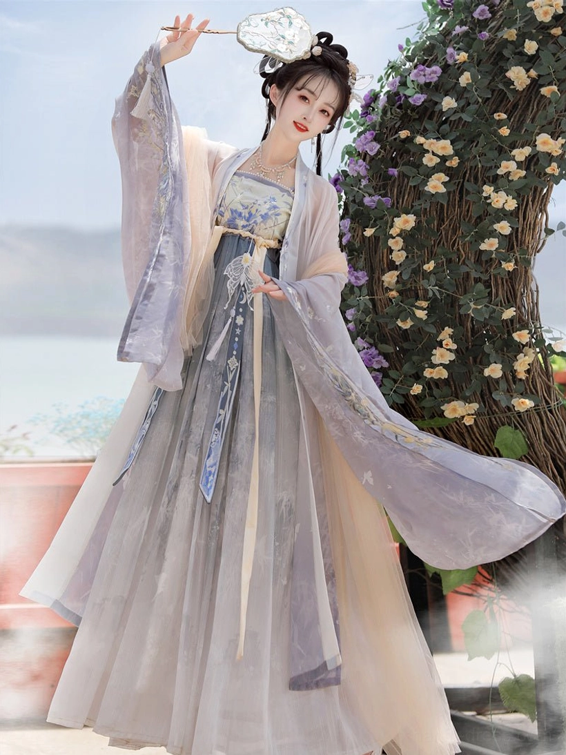 Tang Dynasty inspired Hanfu Heziqun layered dress with embroidered sash and flowing wide sleeves, modeled beside a lakeside flower arch with a traditional round fan