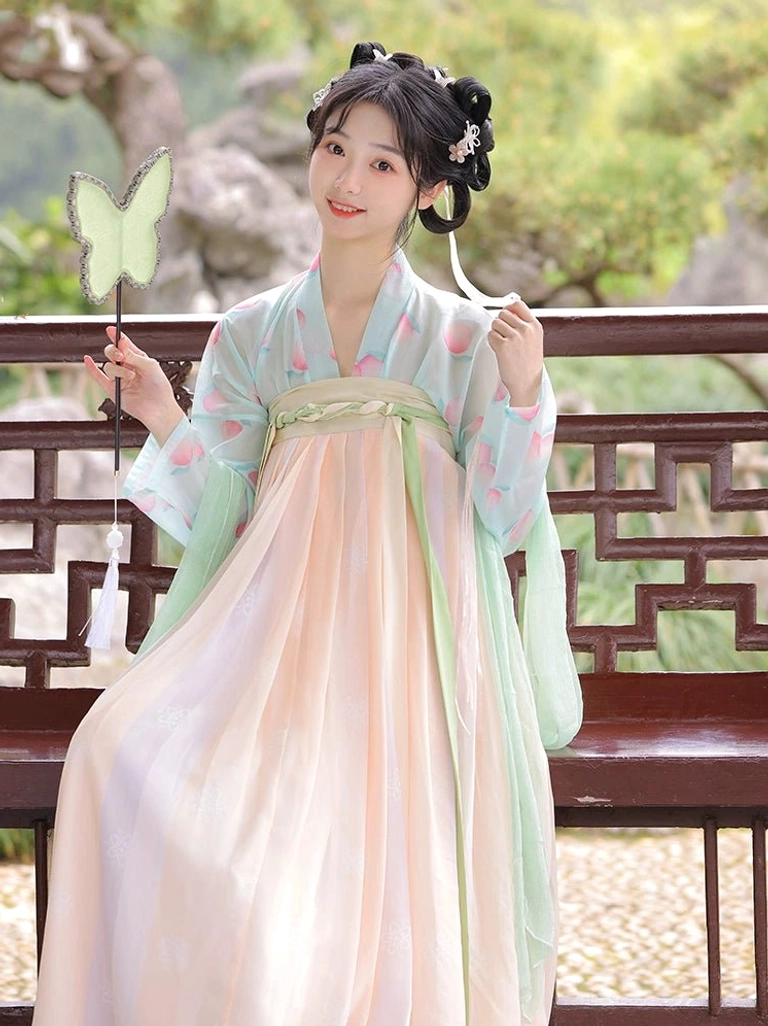 Seated model wearing an apricot gradient Tang Dynasty Hanfu Qixiong Ruqun with a mint green blouse and butterfly-shaped decorative fan in a Chinese garden
