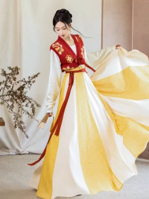 Front three-quarter view of a Tang Dynasty inspired modern Hanfu outfit with red embroidered beizi vest, golden floral details, red waist sash, and flowing yellow and ivory twelve-panel wrap skirt