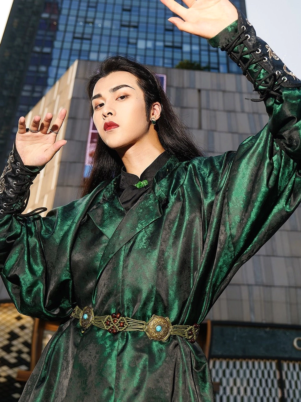 Close-up front view of a model wearing a dark green Tang Dynasty Hanfu robe with oversized batwing sleeves, textured jacquard fabric, round collar, lace-up embroidered cuffs, and decorative metal waist belt