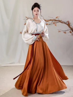 Full body view of a modern Tang Dynasty Hanfu two piece set with ivory jacquard round collar top, light blue trim, burnt orange pleated wrap skirt, and deep red waist sash