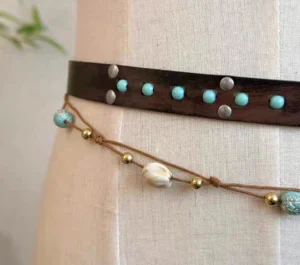 Close-up detail of a Tang-inspired Hanfu waist belt showing brown leather, silver fasteners, turquoise studs, golden beads, white shell pendants, and retro blue decorative beads