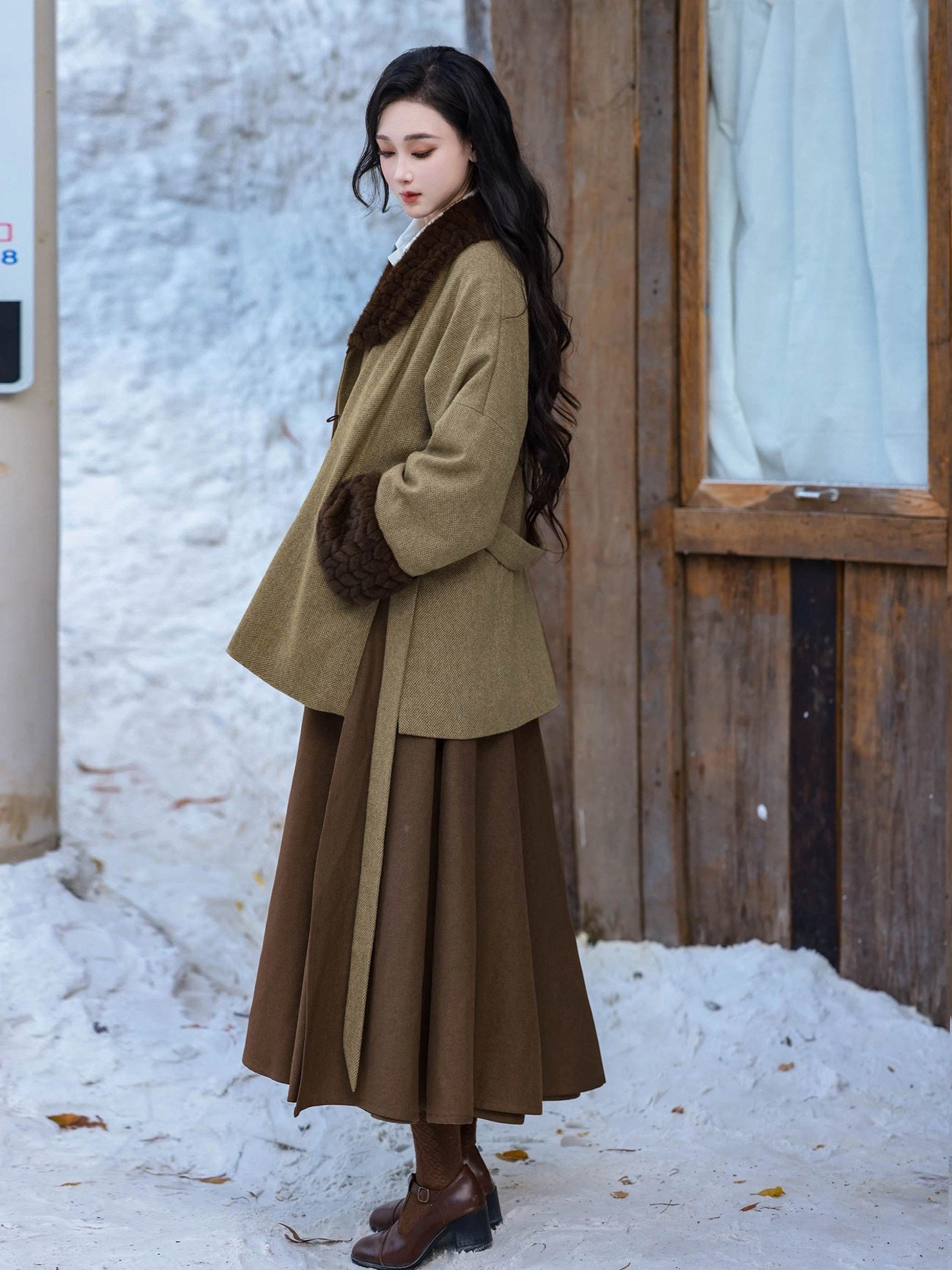 Full-length side view of a Tang Dynasty inspired winter hanfu outfit with olive wool jacket and flowing dark brown pleated skirt in snow