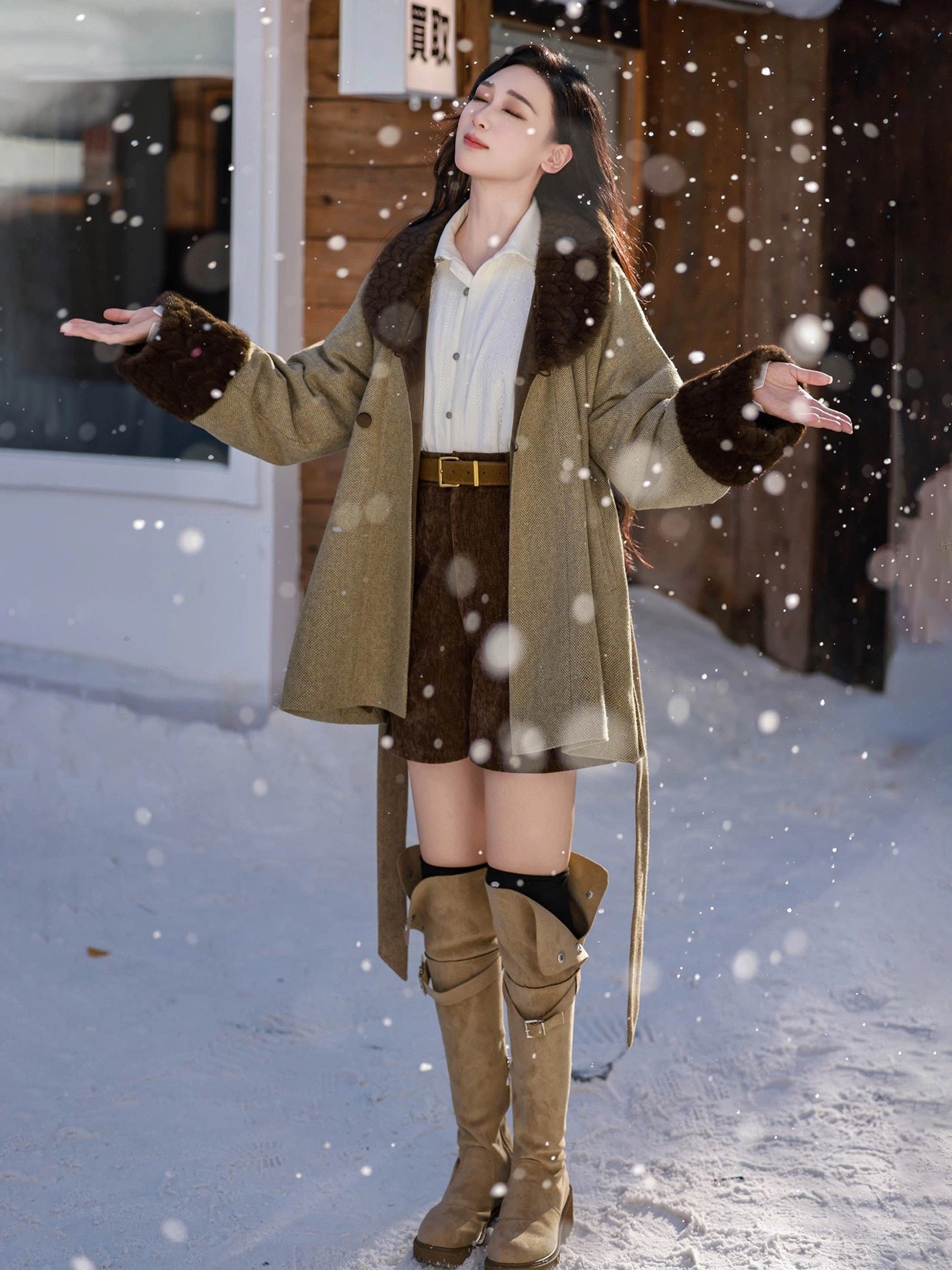 Model wearing an olive green Tang Dynasty inspired winter wool hanfu jacket with dark brown fuzzy trim, brown shorts, and tall boots in a snowy outdoor setting