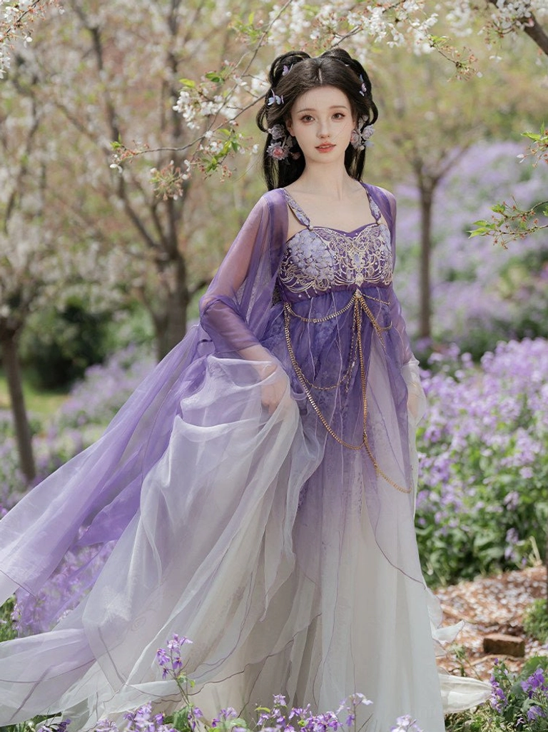 Front view of a Tang Dynasty Hezi Hanfu dress with purple to ivory gradient skirt, embroidered bust top, gold waist chains, and sheer wide sleeve jacket in a flowering garden