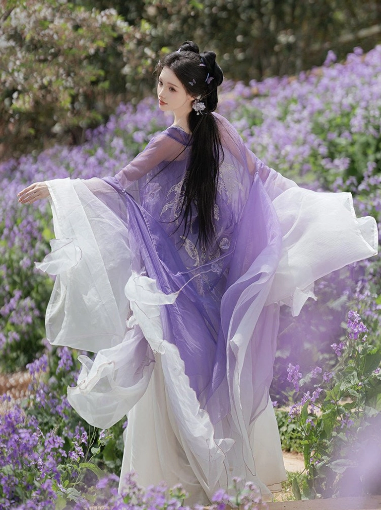 Back three-quarter view of a Tang Dynasty Hezi Hanfu outfit showing fluttering sheer wide sleeves, layered purple and cream skirt, and flowing outer jacket