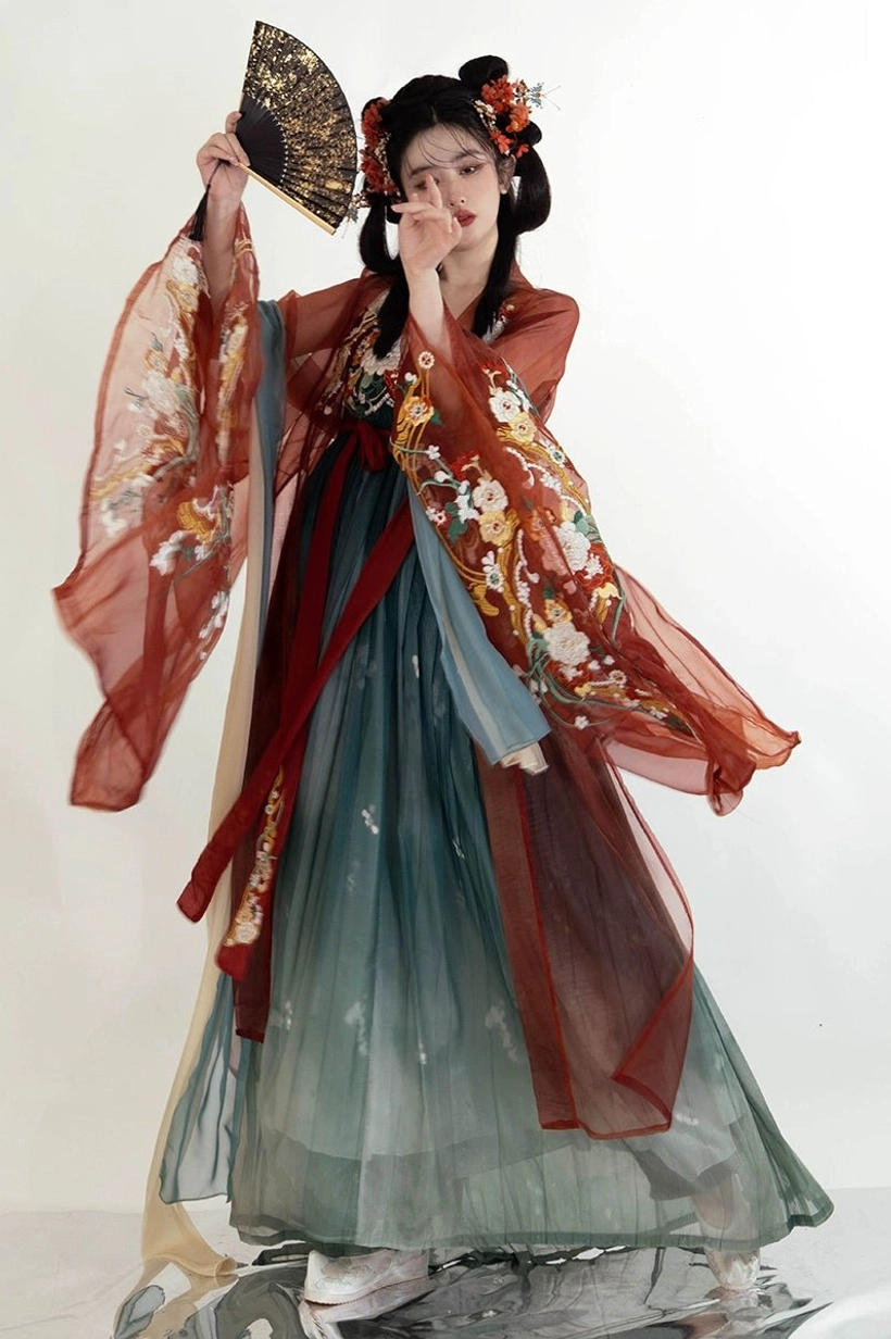 Front side view of a Tang Dynasty Heziqun Hanfu outfit with embroidered sheer wide sleeves, rust red outer robe, dark teal pleated skirt, and traditional floral accessories