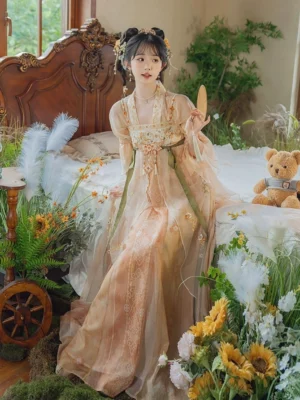 Three-quarter front view of a peach-apricot gradient Tang Dynasty inspired modern Hanfu dress with floral embroidery, green waist sashes, ruffled puff sleeves, and layered organza skirt