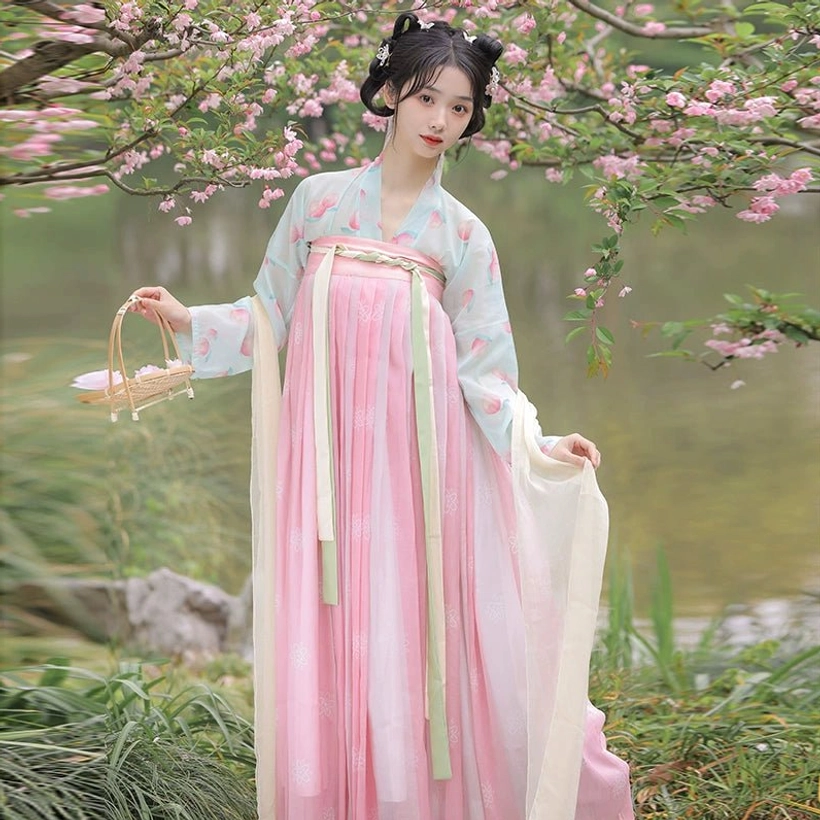 Front close-up of a Tang Dynasty Qixiong Ruqun Hanfu with a mint green printed blouse, pink skirt, green waist ribbons, wicker basket, and elegant classical hairstyle