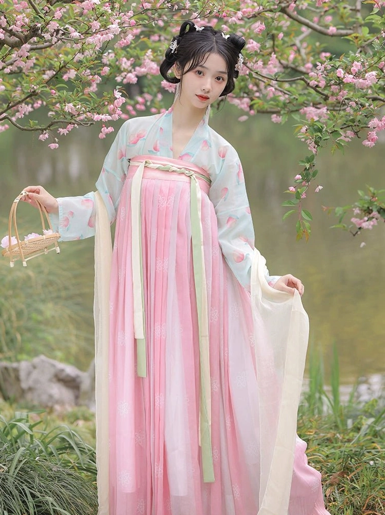 Tang Dynasty style Qixiong Ruqun Hanfu in a peach blossom grove with a mint green printed top, pink gradient pleated skirt, and classical double bun hairstyle