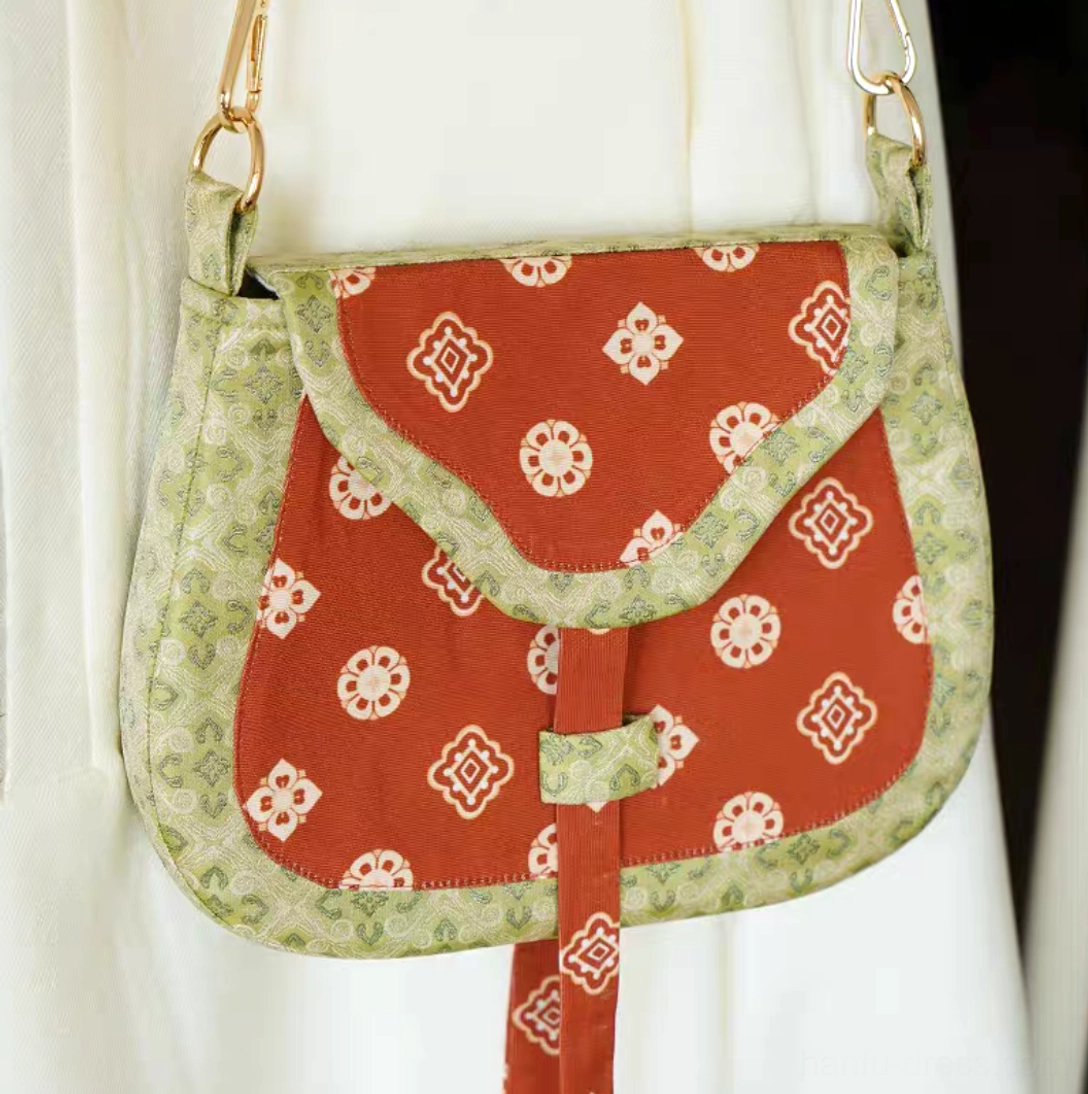 Tang Dynasty inspired red floral Chinese canvas crossbody bag displayed from a front-right angle with patterned trim, flap closure, and gold adjustable shoulder strap hardware