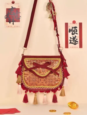 Tang-inspired imperial brocade tassel Chinese crossbody bag in burgundy and gold displayed on a Lunar New Year themed flat lay with calligraphy and gold ingots