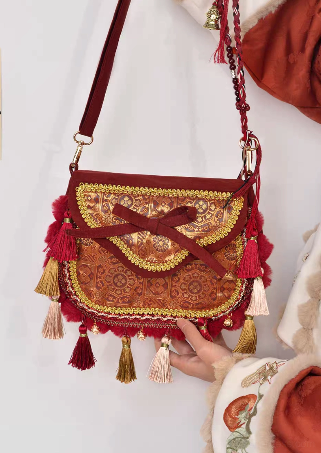 Handheld view of Tang-inspired burgundy brocade Chinese crossbody bag with adjustable shoulder strap, gold trim, front bow and tassel decorations