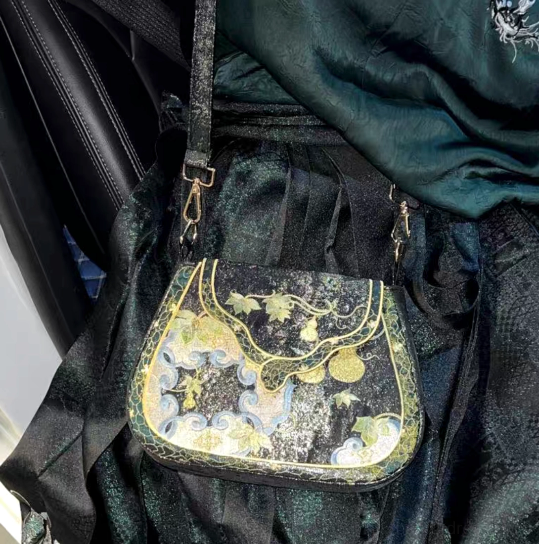 Front close-up of Tang-inspired black Chinese embroidered crossbody bag styled with dark green traditional Hanfu clothing