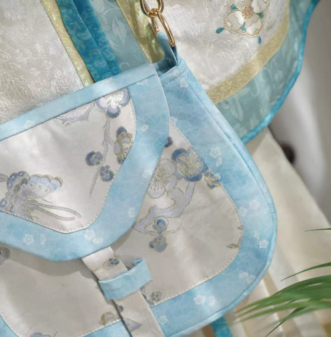 Close-up front view of a Tang-inspired Chinese crossbody bag with delicate blue floral and rabbit embroidery, sky-blue fabric edging, and traditional front strap fastener