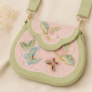 Tang-inspired butterfly embroidered Chinese crossbody bag in blush pink with sage green trim, cloud-shaped flap, gold-tone hardware and multicolor butterfly embroidery