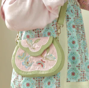 Tang-inspired butterfly embroidered Chinese crossbody bag worn with Hanfu traditional clothing, showing the blush pink saddle bag and sage green trim